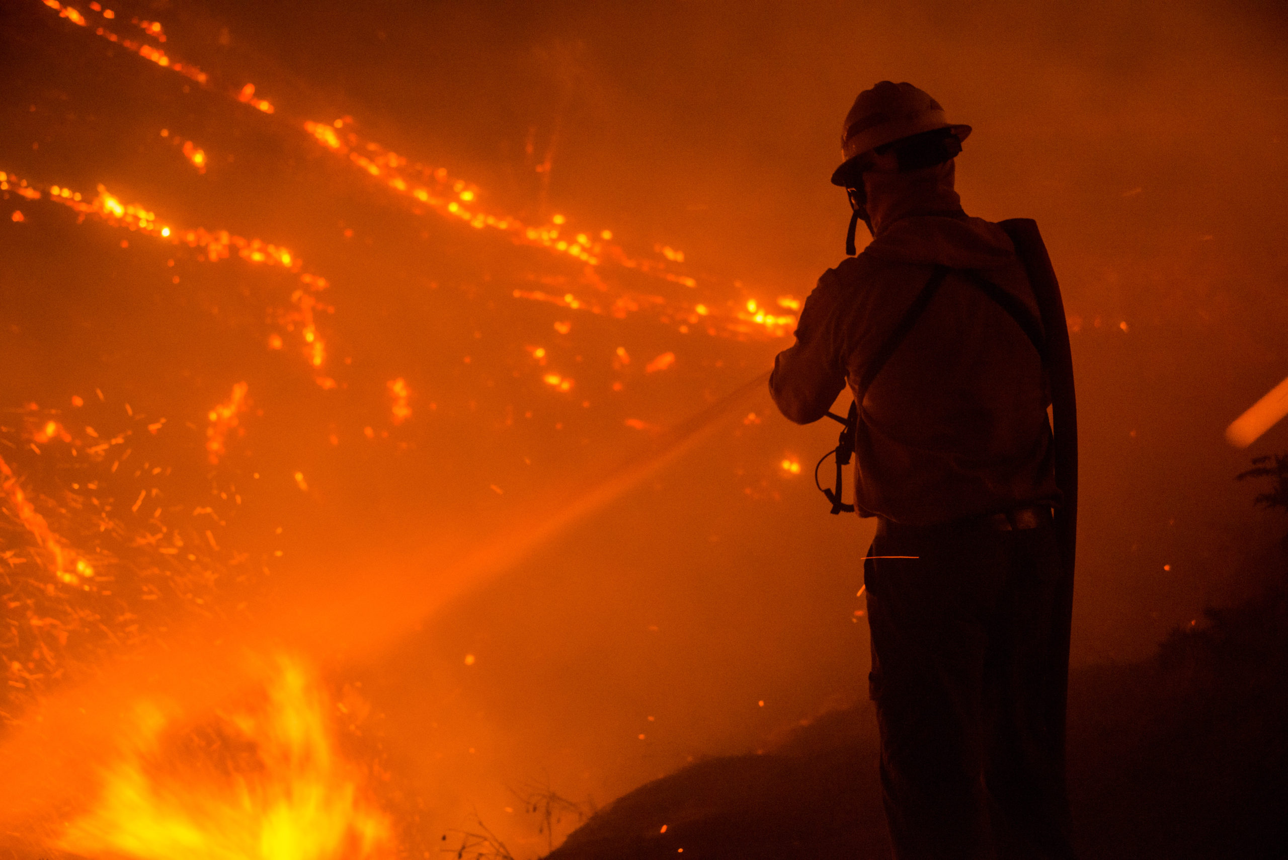 Wildland Firefighter spraying an active wildfire with a hose over his shoulder